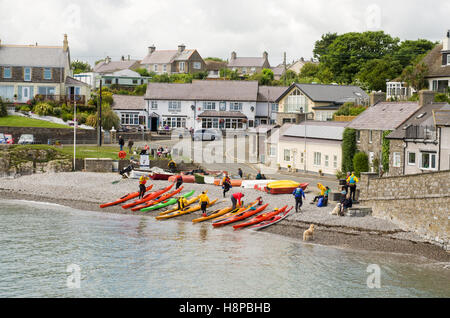 Kanus und Kanuten auf der Kies Strand Moelfre Bucht, in der Ortschaft Moelfre, Anglesey, Wales Stockfoto