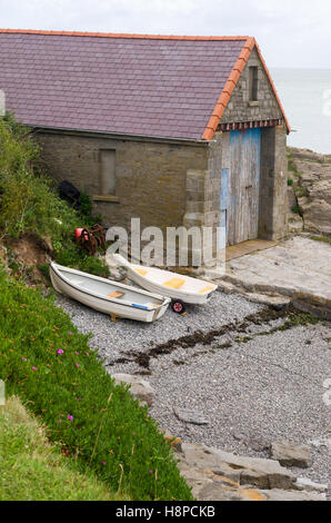Stein-Bootshaus und kleine Boote auf einem Kiesstrand in das Dorf Moelfre, Isle of Anglesey, North Wales, U.K Stockfoto