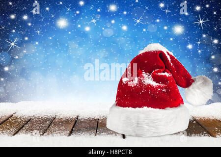 Weihnachten Xmas Hintergrund mit Weihnachtsmann Mütze Kappe auf verschneiten Holzbohlen vor blaue Nacht Himmel, Sterne und Schneeflocken Stockfoto