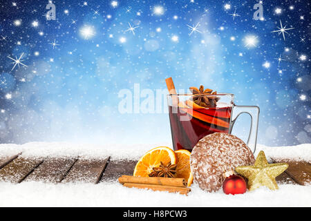 würzigen Glühwein auf verschneiten Holzbohlen vor blauen Nachthimmel mit Sternen und Schneeflocken Hintergrund Stockfoto