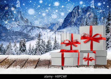 Weihnachten Xmas Hintergrund mit roten Silberband Geschenk Geschenkkartons auf verschneiten Holzbohlen vor Wald Berglandschaft Stockfoto