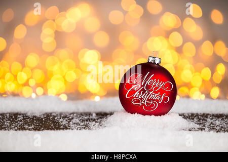 rot Frohe Weihnachten Weihnachten Christbaumkugel Kugel auf verschneiten Holzbrett vor vielen hellen Lichter Bokeh Hintergrund beleuchtet Stockfoto