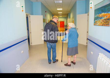 Reifer Mann helfen alte Frau zu Fuß entlang der Passage in einem Pflegeheim. Stockfoto