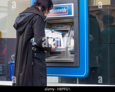 Ein Mann gekleidet in schwarz aus einer Nationwide Building Society ATM oder Geldautomaten Bargeld abheben Stockfoto