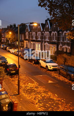 Herbst Blätter bedecken die Bürgersteige und Straßen in einer typischen Süd-London-Straße nach Einbruch der Dunkelheit auf eine nasse Nacht. Zeigt Straße Buckel. Stockfoto