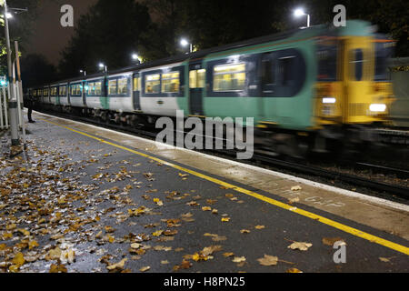 Herbstblätter auf der Strecke und die Plattform am Bahnhof South London, wie ein Zug kommt. Abend-Bild, nass. Stockfoto