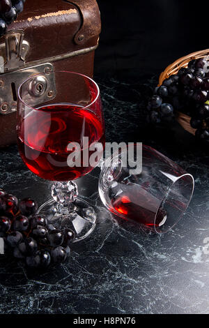 Ein Glas Rotwein und leeres Glas auf dunklem Marmor. Blaue reife Trauben auf dunklem Marmor. Reife Trauben Stockfoto