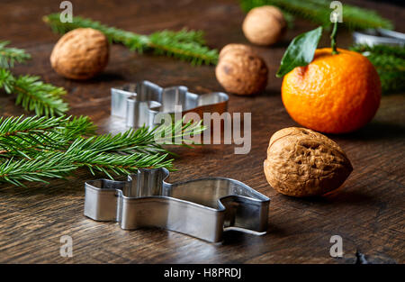 Thema Weihnachten mit Tannenzweigen Baum, Orange, Walnüssen und Ausstechformen auf Holztisch Stockfoto