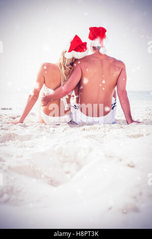 Zusammengesetztes Bild der Rückansicht des Paares Santa Hut am Strand Stockfoto