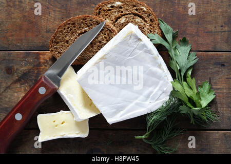 Stück französischer Brie Käse in der Nähe von Messer und Brot auf alten hölzernen Hintergrund Stockfoto