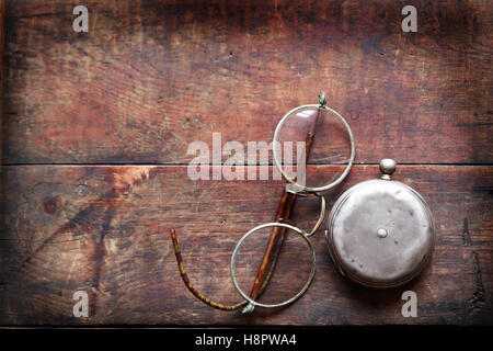 Alte Brille in der Nähe von geschlossenen Taschenuhr auf hölzernen Hintergrund Stockfoto