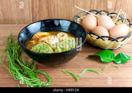 Scharf-saure Suppe Curry mit Garnelen und Acacia Pennata Omelett. In schwarzer Schale auf Holztisch. Stockfoto