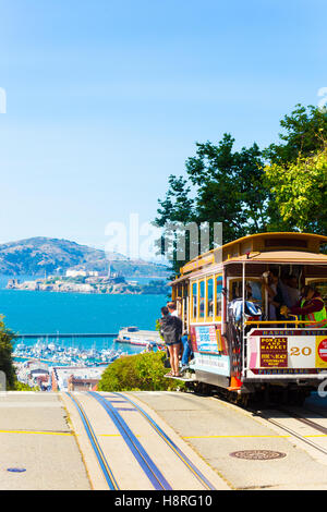 Eine ikonische Seilbahn voller Passagiere auf der Kuppe des Hyde Street gehen über die Kante in Richtung der Blick auf Alcatraz-Insel in der Stockfoto