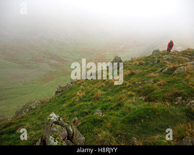 Walker im roten Mantel nach unten Riggindale, eingehüllt in eine Wolke von rauen Felsen an der High Street über Haweswater Seenplatte UK Stockfoto