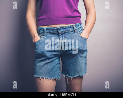 Eine junge Frau trägt Jeans-Shorts posiert mit ihren Händen in den Taschen Stockfoto