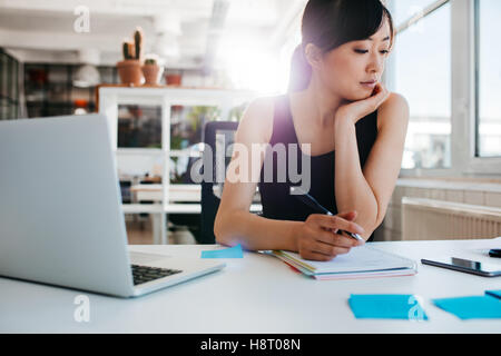 Aufnahme des jungen Asiatin an ihrem Schreibtisch arbeiten schreiben von Notizen. Geschäftsfrau an ihrem Arbeitsplatz. Stockfoto
