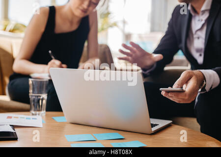Schuss von Geschäftspartnern zusammenarbeiten auf Laptop im Büro. Mann, Mobiltelefon und Frau Notizen schreiben. Stockfoto
