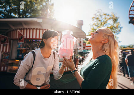 Schuss von glücklich Freundinnen im Vergnügungspark Zuckerwatte essen. Zwei junge Frauen genießen einen Tag im Freizeitpark. Stockfoto