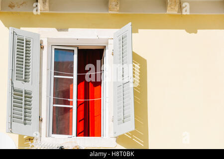 Ein offenes Fenster mit Fensterläden aus Holz und rote Vorhänge an einem sonnigen Tag Stockfoto