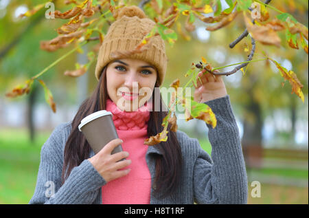 Schöne junge Frau mit Hut Mütze im Park im Herbst halten zum Mitnehmen Kaffeetasse, lächelnd. Stockfoto