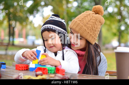 Junge Frau mit ihrem Kind spielen mit bunten Kunststoffblöcke im freien Stockfoto
