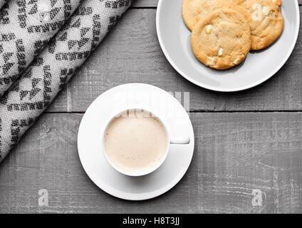 Tasse Cappuccino mit grauen Wollschal und Keksen auf hölzernen Hintergrund Stockfoto