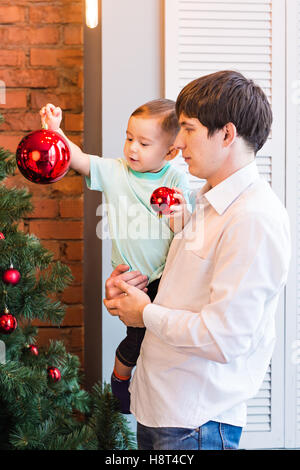 Sohn und Vater schmücken den Weihnachtsbaum zu Hause im Wohnzimmer Stockfoto