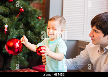 Sohn und Vater schmücken den Weihnachtsbaum zu Hause im Wohnzimmer Stockfoto