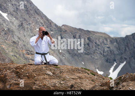 Der Mann in einem Kimono sitzt im Lotussitz auf Berg- und aufnehmen von Bildern die Kamera. Stockfoto