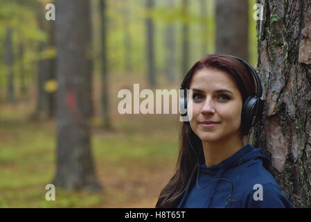 Schöne und glückliche Mädchen hört Musik im Kopfhörer in der Natur. Herbst-Forrest im Hintergrund Stockfoto