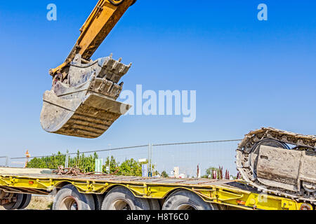 Schwere Bagger klettert es auf niedrige Plattform Anhänger über rückseitige Rampe, trägt zwei Eimer ineinander eingefügt. Stockfoto