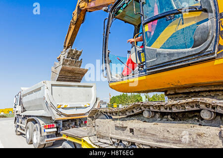 Schwere Bagger klettert es auf niedrige Plattform Anhänger über rückseitige Rampe, trägt zwei Eimer ineinander eingefügt. Stockfoto