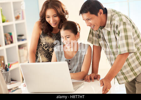 Stolze Eltern betrachten, was ihre Tochter auf ihrem Laptop zu ihnen zeigt. Stockfoto