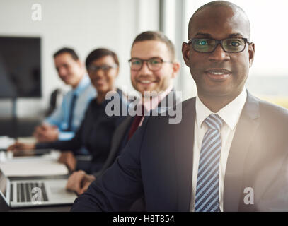 Freundlichen zuversichtlich afrikanischen Geschäftsmann in einem Management-Meeting mit einer Gruppe von Rassen Kollegen lächelnd in die Kamera Stockfoto