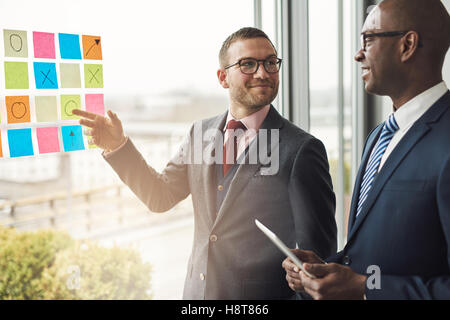Zwei Geschäftsleute vor einem hellen Fenster mit Bördel lächelnd wie versuchen, ein Problem auf bunten Memos zu lösen Stu Stockfoto