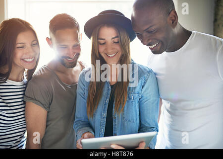 Heterogene Gruppe von vier erwachsenen Männern und Frauen lachen eng beieinander stehen, um einen Tabletcomputer Stockfoto