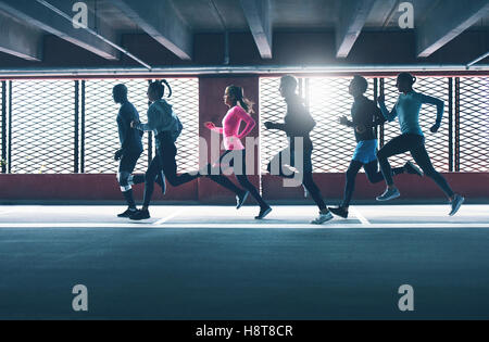 Gruppe von vielfältigen städtischen Läufer sprinten über den Rahmen in ein Parkhaus als sie Training Hintergrundbeleuchtung von der Sonne durch ein Gri Stockfoto
