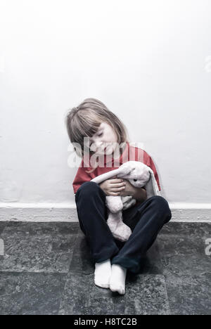 Ein Junge vier Jahre alten kleines Mädchen sitzen auf dem Boden mit einem alten Spielzeug suchen traurig. Stockfoto