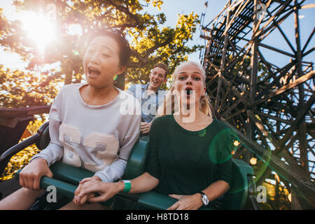 Schuss von jungen Freunden genießen, fahren Achterbahn im Freizeitpark. Junge Leute, die Spaß auf Achterbahn. Stockfoto