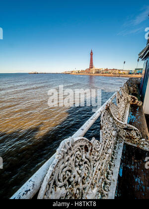 Traditionelle Gusseisen Sitze in einem Zustand des Verfalls am Pier mit Blackpool Tower in Ferne, Blackpool, Lancashire, UK. Stockfoto