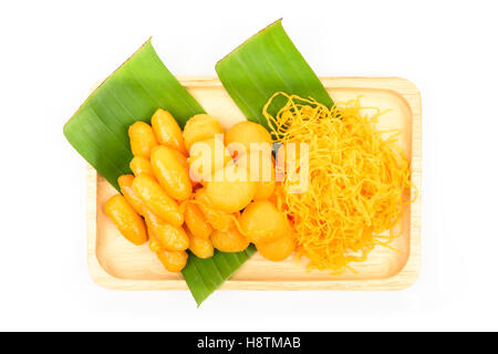 Thailändische Süßspeise (Med Khun, Yod Thong, Foy Thong) auf einer Holzplatte mit grünen Bananenblatt isoliert auf weißem Hintergrund, Thai Stockfoto