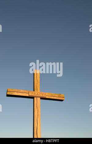 Einfachen christlichen Holzkreuz mit dem Wort "Frieden" auf eine angehängten Zeichen vor einem strahlend blauen Himmel. Stockfoto