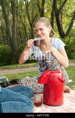 Schöne Mädchen 20-24 Jahre alten ruhen im Park, die grüne frische Gras mit Tasse Kaffee sitzen. Glücklich im Chat ihre Freundin reden und Spaß haben Gras Stockfoto