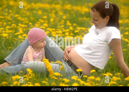 Schwangere Mutter mit einem Baby, Mädchen, in einer Frühlingswiese Stockfoto