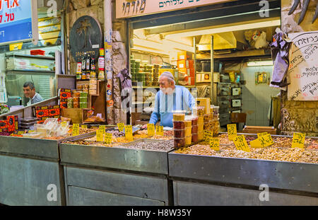 Der senior Händler im Stall der Mahane Yehuda Markt bietet die getrockneten Früchte, Sonnenblumenkerne und verschiedenen Nüssen Stockfoto