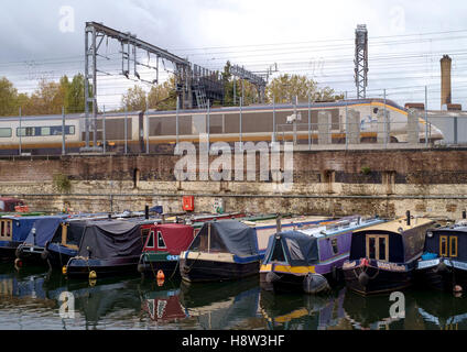 Die Regents Canal in St Pancras in London.  Ein Eurostar-Zug läuft neben einer Kanal-Becken von festgemachten Narrowboats. Stockfoto