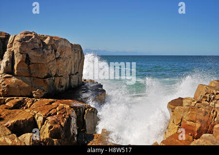 Südafrika: Brechen von Wellen auf dem roten Felsen am Strand von Plettenberg Bay, einer Stadt an der berühmten Garden Route. Stockfoto