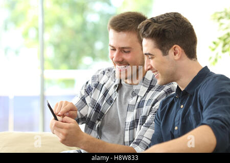 Zwei Freunde beobachten Medieninhalte in ein intelligentes Telefon sitzen auf einer Couch im Wohnzimmer zu Hause Stockfoto