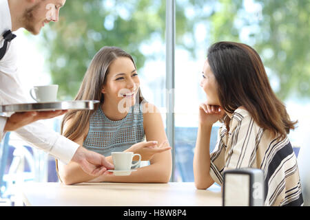 Glückliche Freunde reden suchen einander sitzen in der Tabelle eine Bar mit dem Kellner servieren Tassen Kaffee Stockfoto