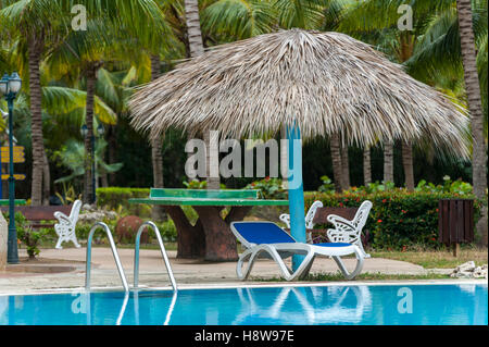 Liegestuhl am Pool von Strohhütte unter Palmen am Pool des Hotels Stockfoto